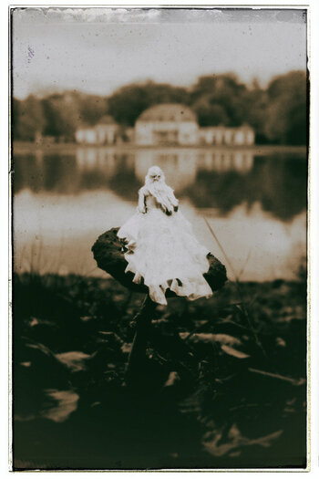 A sepia-toned photograph of a fairy sitting on a mushroom, longingly looking towards a house across the lake.