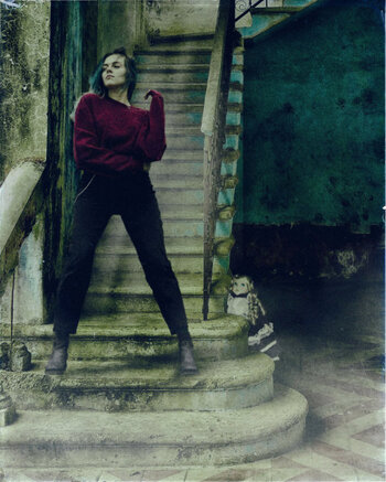 A person standing boldly on a set of stairs and looking out, with a doll hiding behind the staircase